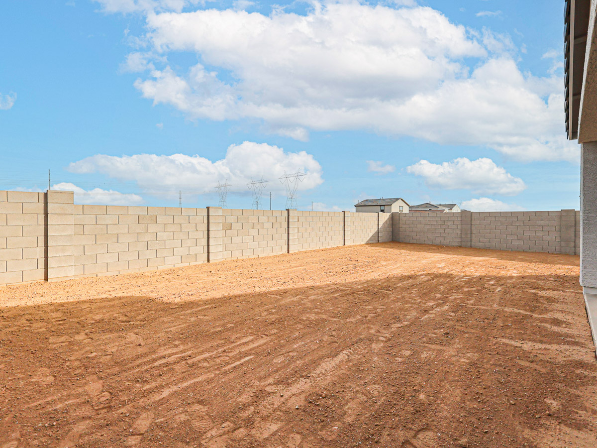 A dirt field with a fence and a building in the background.