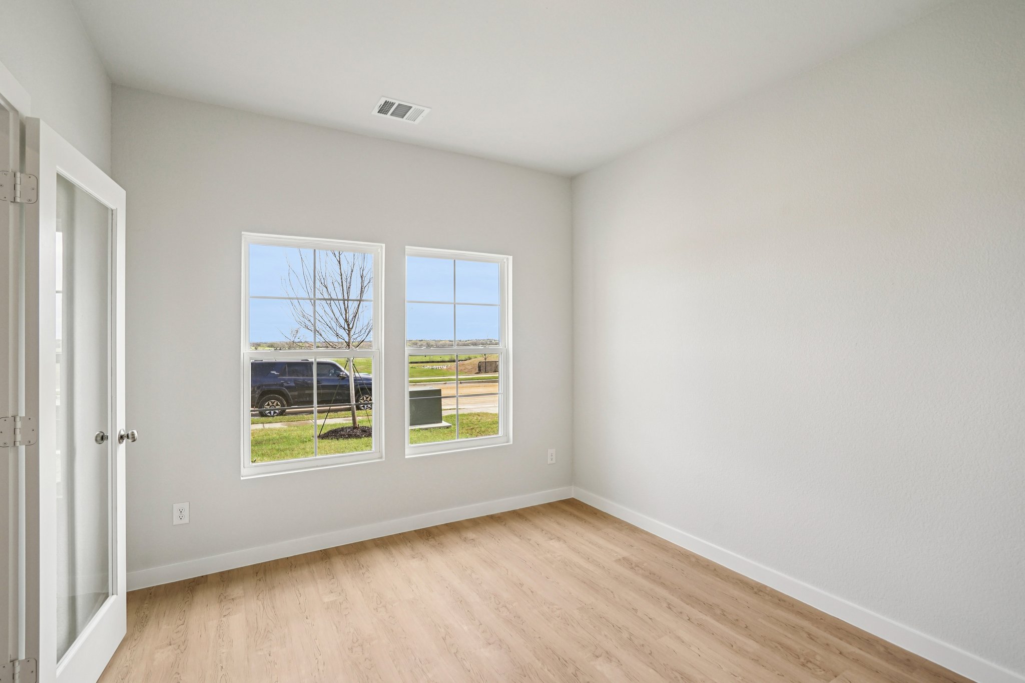 A room with a wood floor and a window with a view of a street and trees.