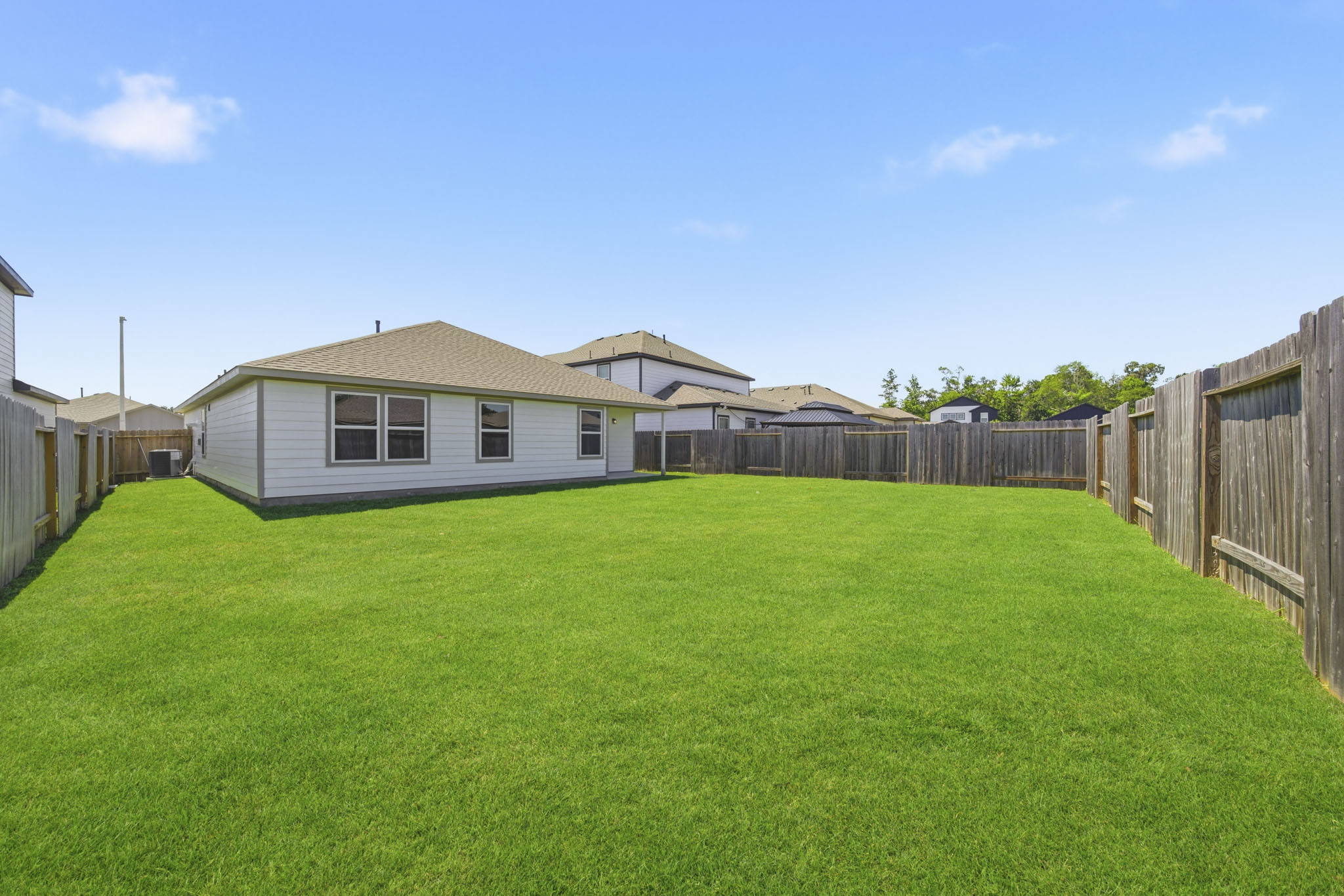 A grassy yard with a fence and houses in the background.
