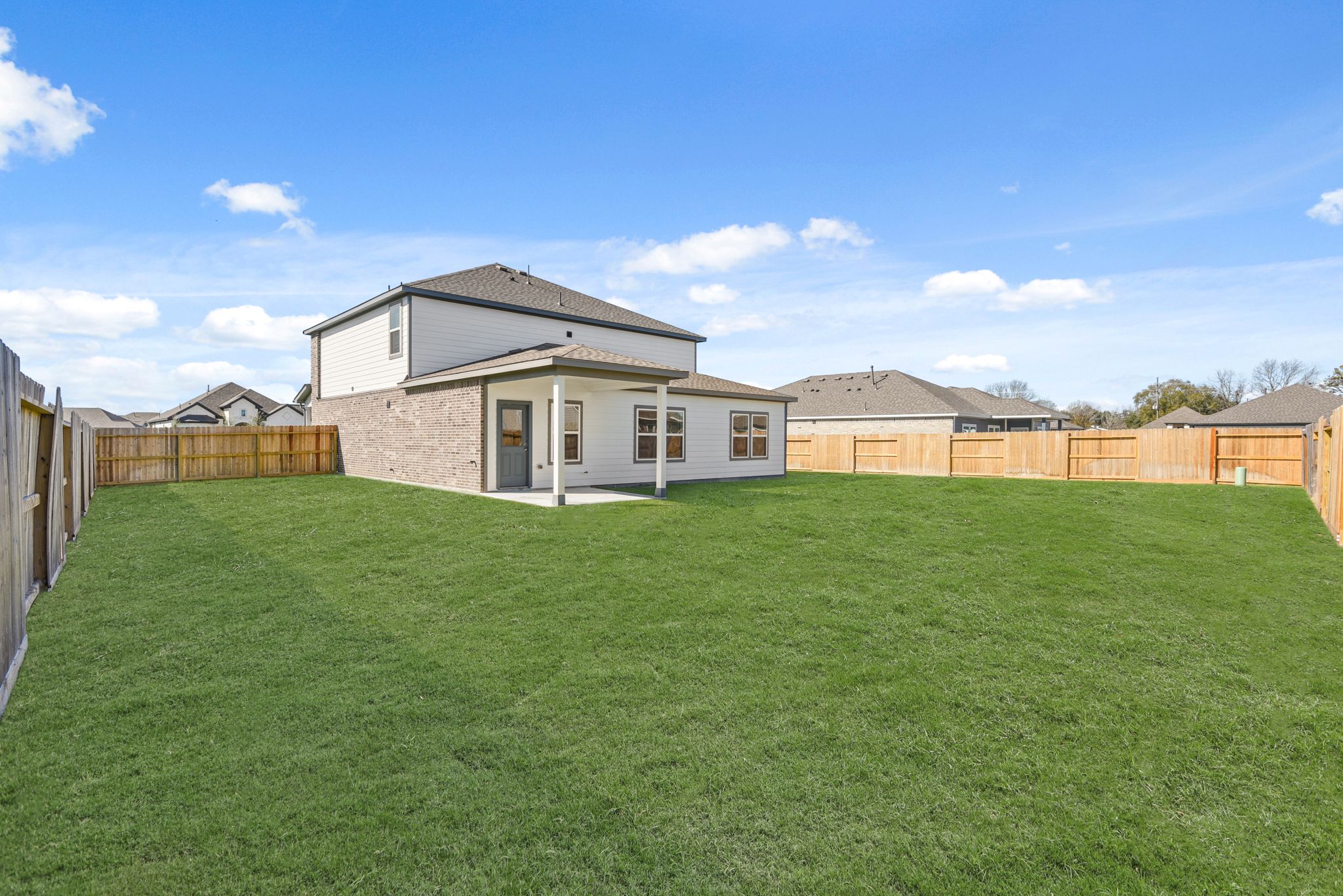 A large green lawn with a fence and a house in the background.