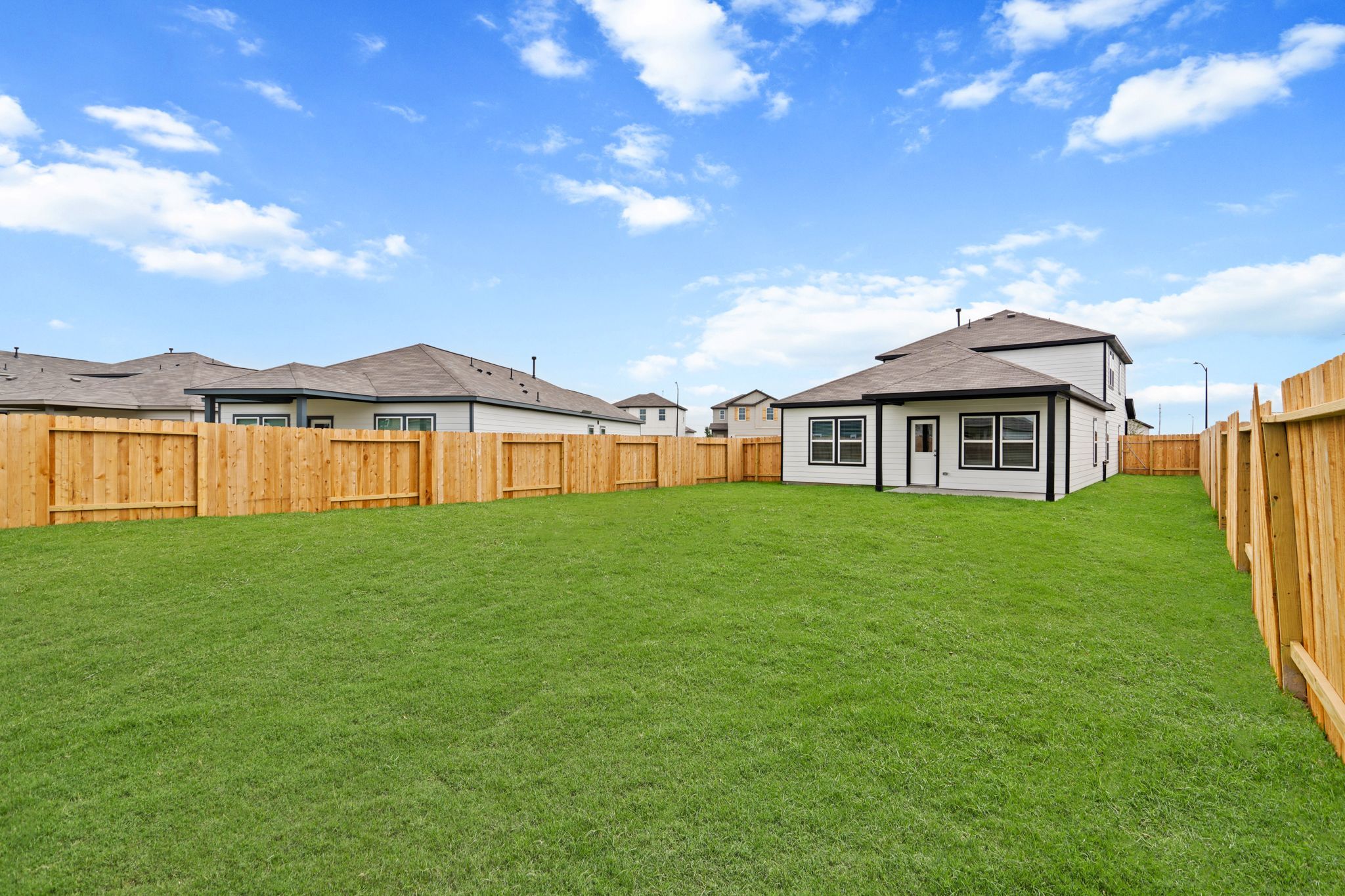 A grassy yard with a fence and a house in the background.