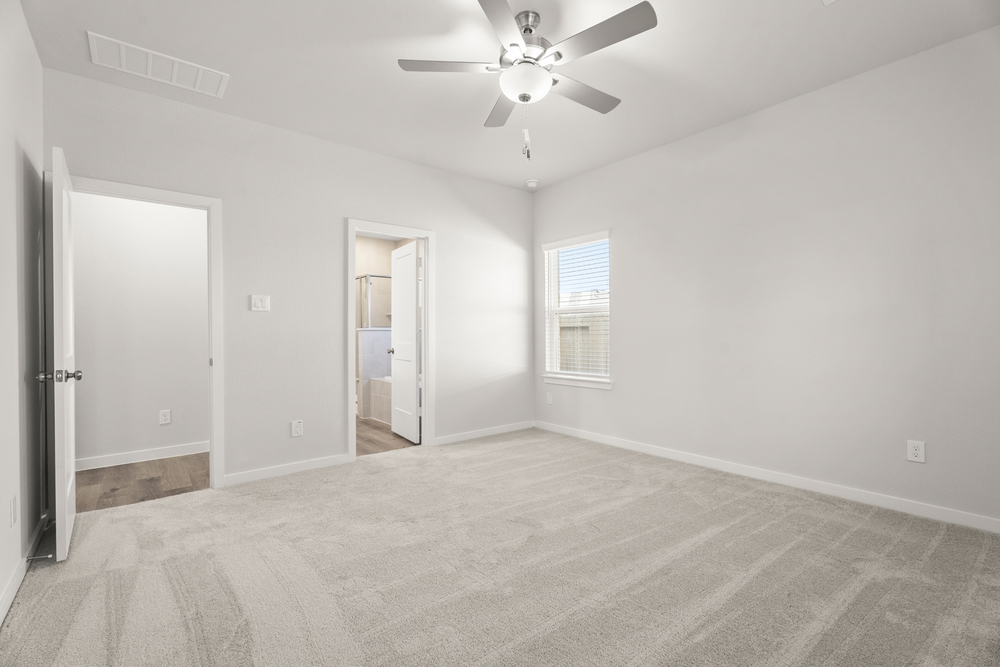 A large empty room with a ceiling fan and a door.
