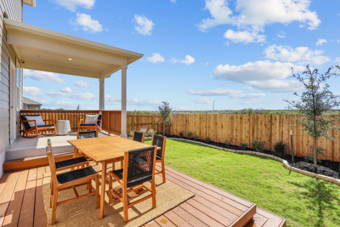 A deck with a table and chairs on it and a grass field in the background.